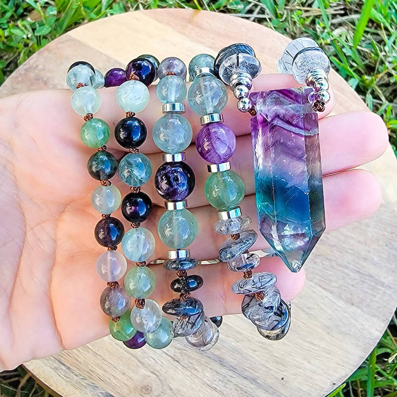Looking for Fluorite Crystal Mala - Handcrafted for Chakra Energy? Shop at Magic Crystals. Wearing, carrying, or meditating with this Flurotie crystal mala can open the mind and heart to higher guidance. Features a combination of Tourmalinated Quartz and Fluorite beads with a double point as a center piece. SHIPS FREE