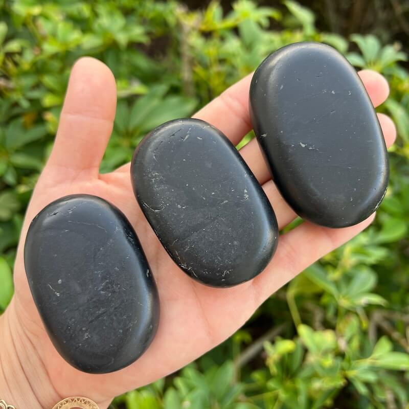 Large natural black Shungite palm stone with smooth polished oval surface on a 
hand.
