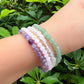 Stacked crystal healing bracelets featuring Green Aventurine, Rose Quartz, Clear Quartz, and Amethyst gemstones worn on wrist outdoors.