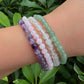 Stacked crystal healing bracelets featuring Green Aventurine, Rose Quartz, Clear Quartz, and Amethyst gemstones worn on wrist outdoors.