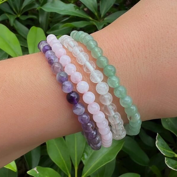 Stacked crystal healing bracelets featuring Green Aventurine, Rose Quartz, Clear Quartz, and Amethyst gemstones worn on wrist outdoors.