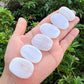 Five smooth, polished white stones arranged in a person's open palm, with a background of green outdoor foliage.