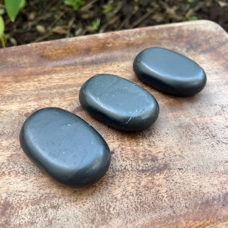 Large natural black Shungite palm stone with smooth polished oval surface on a 
hand from MagicCrystals.com