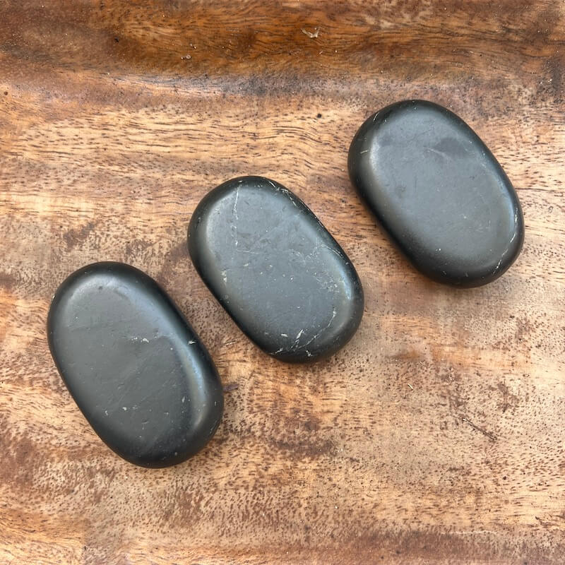 Large black Shungite palm stone with smooth polished oval surface on a 
hand from MagicCrystals.com