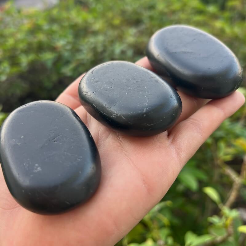 Large black Shungite palm stone with smooth polished oval surface on a 
hand from MagicCrystals.com